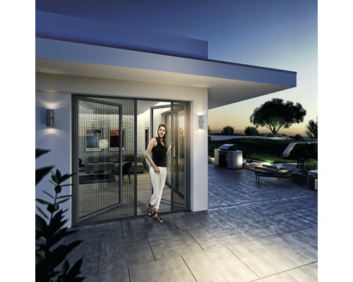 Une femme se tient dans une porte d''entrée moderne avec moustiquaire et vue sur une terrasse avec barbecue.