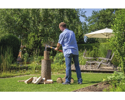 Un homme fend du bois avec une hache dans le jardin.