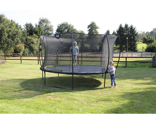Ein EXIT Gartentrampolin mit Sicherheitsnetz steht auf einer Rasenfläche, ein Kind springt, ein anderes steht daneben.
