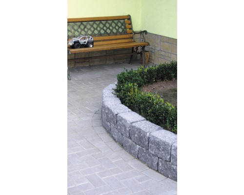 Gartenszene mit einer Steinmauer, einem Weg aus Pflastersteinen und einer Holzbank