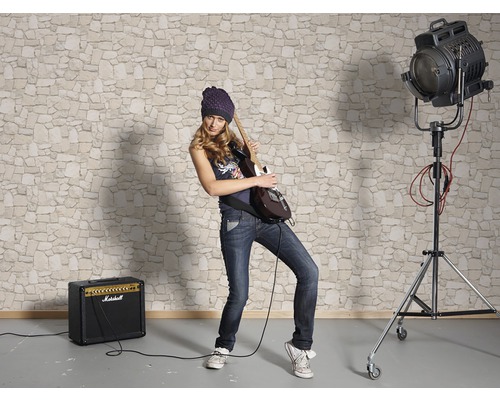 Femme jouant de la guitare devant un papier peint à motif de pierres avec amplificateur et projecteur
