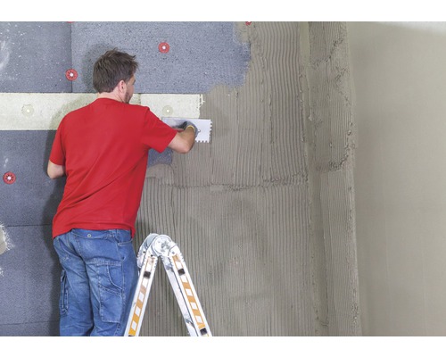 Mann befestigt Dämmplatten an einer Wand mit Kleber und Werkzeug.