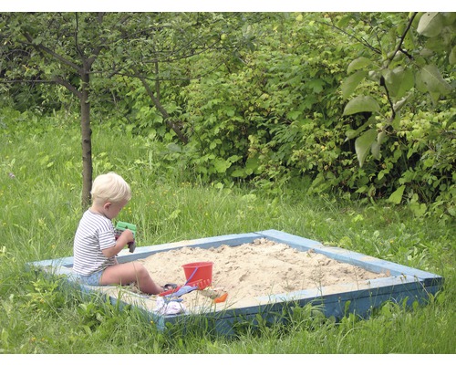 Un garçon joue dans un bac à sable avec des jouets de sable dans le jardin.