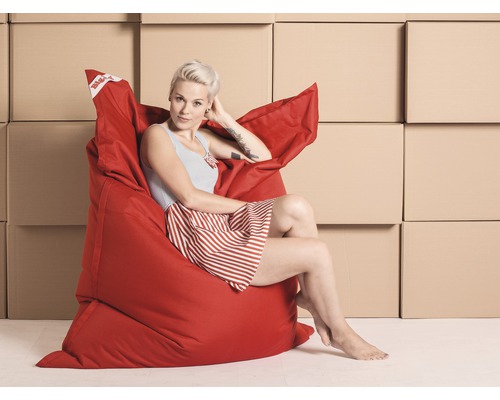 Une femme est assise et détendue dans un pouf rouge devant des cartons.