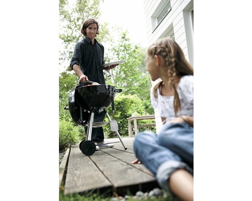 Un homme fait un barbecue avec un barbecue à boules dans le jardin, tandis qu''une fille regarde.