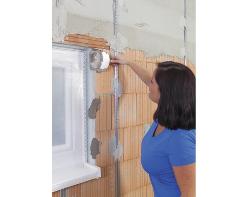 Frau befestigt Dämmstoffplatte an einer Wand in der Nähe eines Fensters.