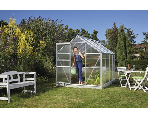 Scène de jardin avec serre, mobilier de jardin et une personne tenant un arrosoir