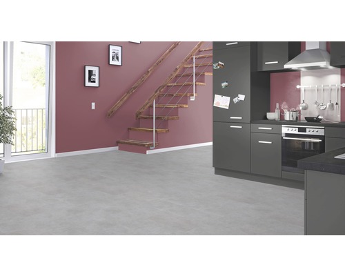 Pièce lumineuse avec kitchenette grise, escalier en bois et grande fenêtre.