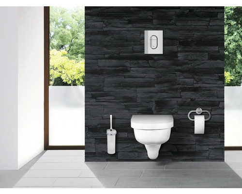 Salle de bains moderne avec WC suspendu, plaque de commande, brosse WC et porte-papier toilette devant un mur en pierre