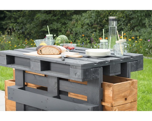 Scène de jardin avec une table en palettes grise avec nourriture et boissons.