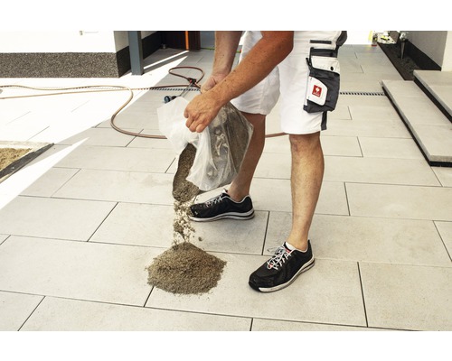 Ein Mann schüttet Fugensand auf einen gepflasterten Bereich im Freien.