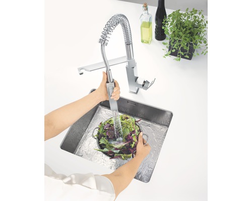 Un évier de cuisine avec une personne lavant des légumes sous un robinet à ressort spiralé.