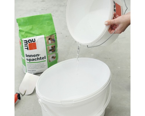 Mélange d''enduit intérieur avec de l''eau dans un seau, y compris une spatule et un sac d''enduit intérieur.