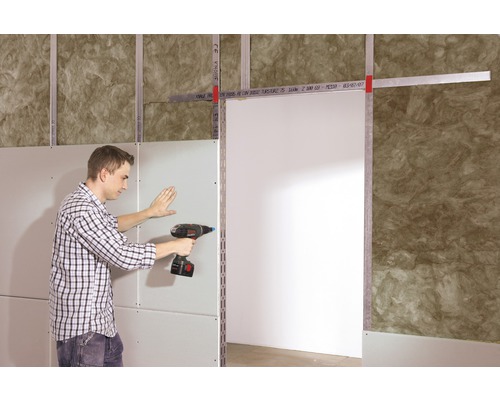 Un homme fixe une plaque de plâtre sur une structure avec une visseuse sans fil.