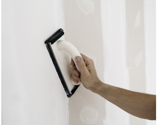 Main ponçant un mur avec une ponceuse manuelle