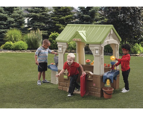 Trois enfants jouent avec une cabane Step2 dans le jardin.