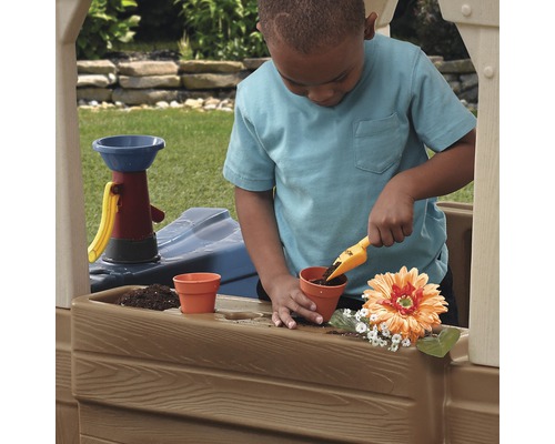 Un enfant joue dans une maisonnette d''extérieur avec une pelle et des pots de fleurs.