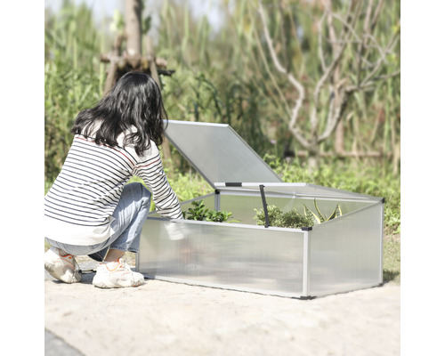 Une femme se penche vers un châssis de couche avec un couvercle ouvert dans le jardin.