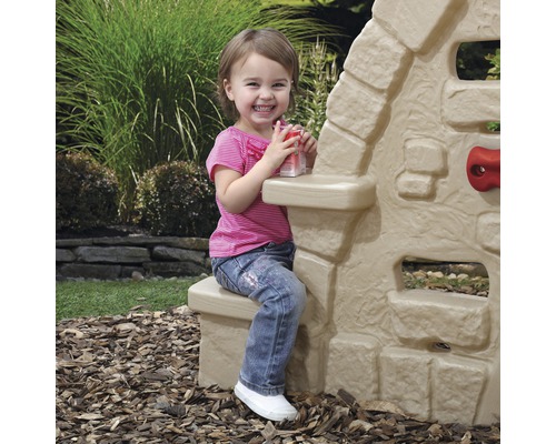Une petite fille est assise près d''une cabane de jeu pour enfants dans le jardin.