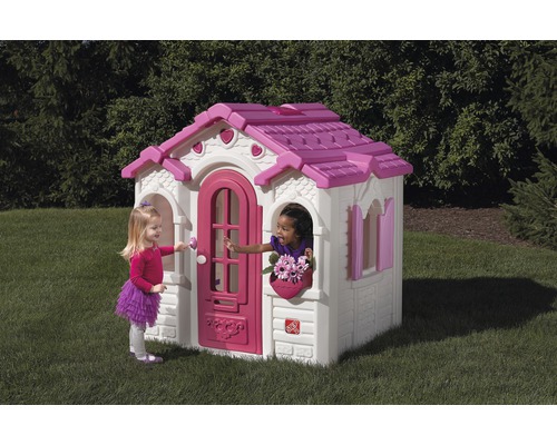 Maisonnette en plastique avec porte et fenêtres dans le jardin, deux enfants qui jouent