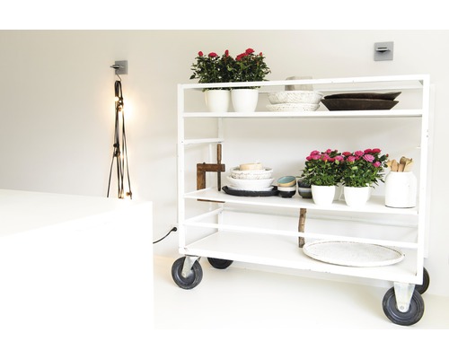 Ein weisses Rollregal mit Blumenschalen, Schüsseln und dekorativen Gegenständen in einem hellen Raum.