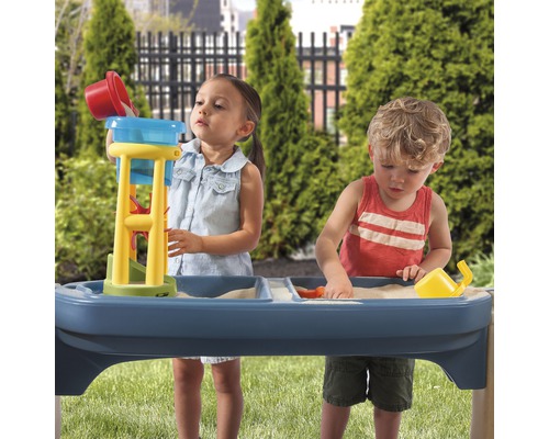 Des enfants jouent avec une table à sable et à eau dans le jardin.