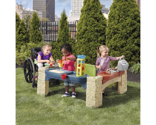 Trois enfants jouent avec une table de jeu dans le jardin. Un enfant est en fauteuil roulant.