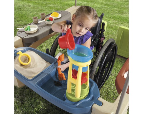 Fille en fauteuil roulant jouant avec une table de jeu pour eau et sable à l''extérieur