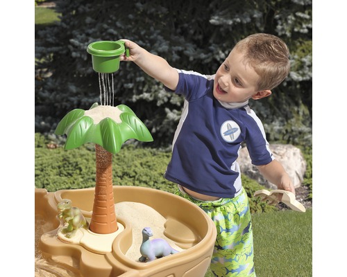 Un enfant joue avec une table de sable et d''eau sur le thème des dinosaures à l''extérieur.