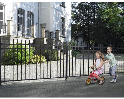 Schwarzer Metallzaun vor einem Gebäude mit spielenden Kindern