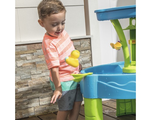 Un enfant joue avec un jeu d''eau bleu et vert à l''extérieur.