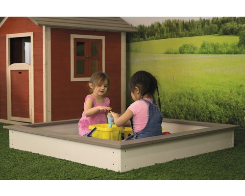 Deux enfants jouent dans un bac à sable devant une cabane de jeu et un papier peint de paysage.