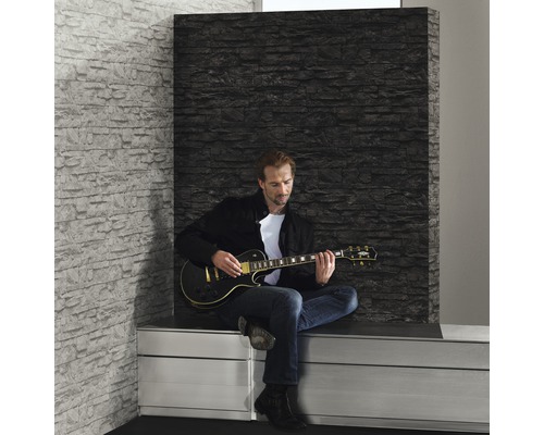 Szene mit Mann, der auf einer E-Gitarre vor einer Wandpaneele mit Steinoptik spielt