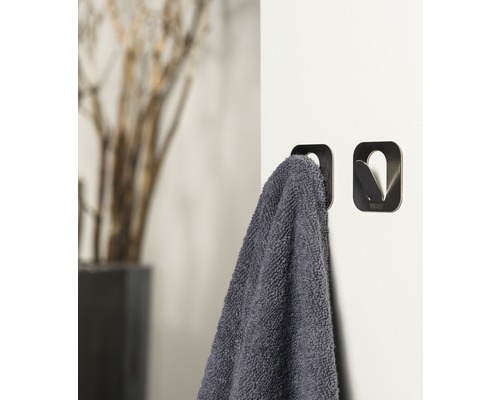 Deux crochets à serviettes en métal sur un mur blanc, l''un avec une serviette grise