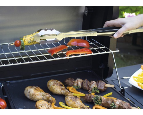 Aufnahme eines Grills mit Grillgut und einer Person mit Grillzange der Marke Campingaz.