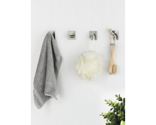 Drei Wandhaken mit Handtuch, Duschball und Bürste an einer Wand