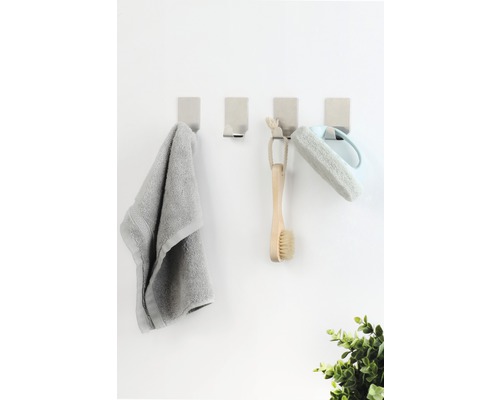Quatre patères avec serviette, brosse et éponge de bain sur un mur