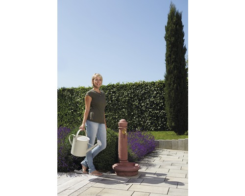 Frau mit Giesskanne neben einem Gartenbrunnen auf einer Terrasse