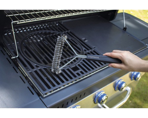 Une personne nettoie une grille de barbecue avec une brosse à gril de la marque Campingaz.