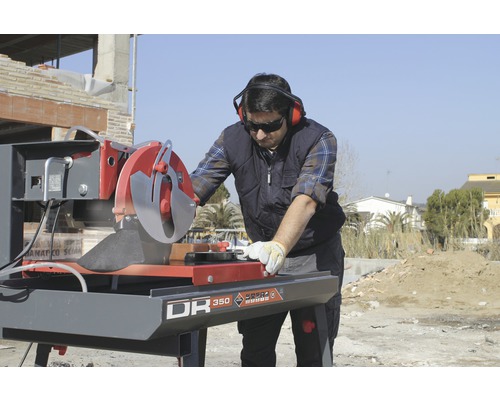 Un homme utilise une carreleuse sur un chantier, portant des vêtements de protection.