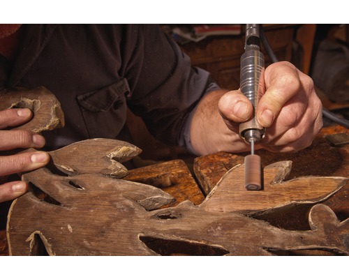 Artisan travaillant des sculptures en bois avec un outil rotatif.