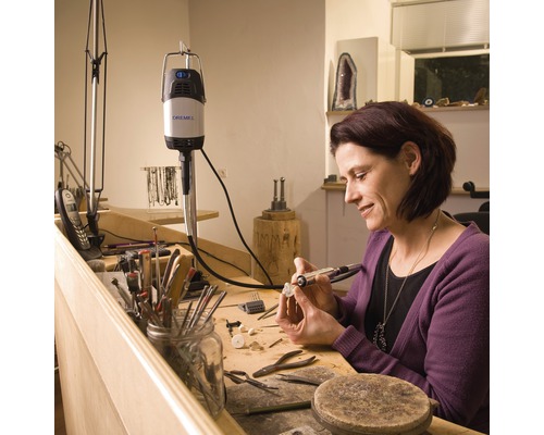 Femme travaille sur une pièce sur un établi avec un outil multifonction Dremel