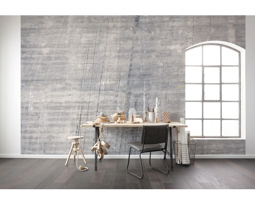 Wohnraum mit grauer Betonwand, Schreibtisch, Stuhl und großem Fenster für eine helle und moderne Atmosphäre.