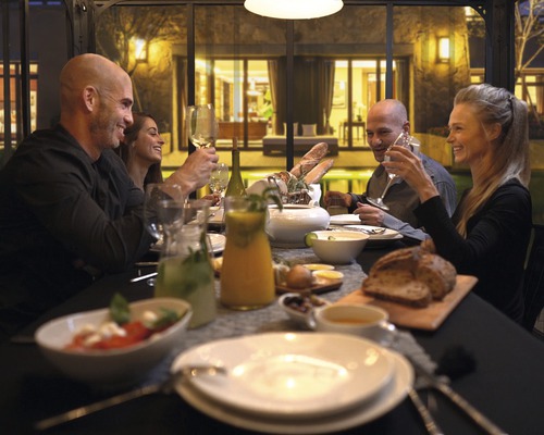 Groupe de personnes assises à une table avec de la nourriture et des boissons dans une véranda.
