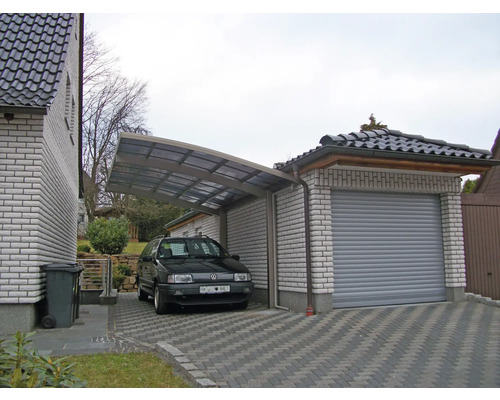 Carport und Garage aus Stein mit gepflasterter Zufahrt und parkendem Auto