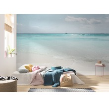 Salon avec papier peint photo représentant un paysage marin avec une plage et un voilier.