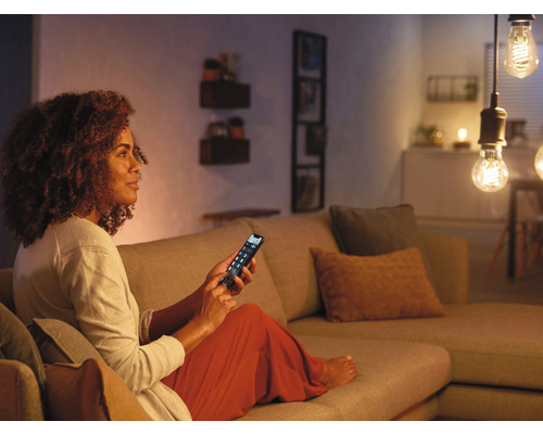 Frau bedient Smart Home Beleuchtung mit dem Mobiltelefon auf dem Sofa