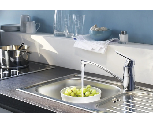 Robinet d''évier avec de l''eau qui coule dans un évier en acier inoxydable rempli de raisins dans une cuisine