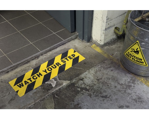 Szene mit einem Schild, das vor einer Stufe warnt und einem Eimer mit einem Warnhinweis vor nassen Böden.