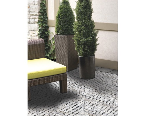 Terrasse avec dalles de sol aspect galets, un fauteuil en rotin avec coussin et plantes en pot